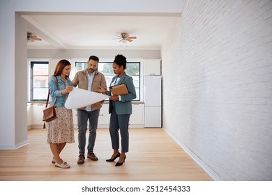 Mid adult couple analyzing blueprints with real estate agent during open house day. Copy space. - Powered by Shutterstock