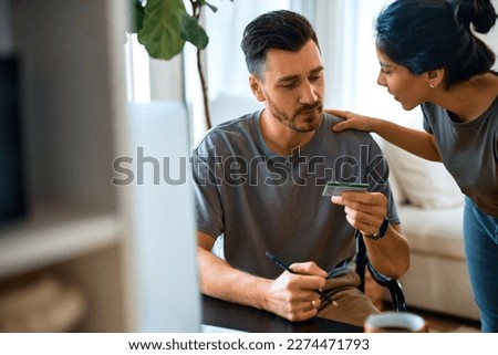 Mid adult couple communicating while using credit card and checking their bank account at home.
