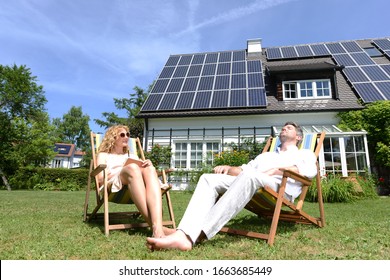 Mid adult couple in deckchairs in garden of solar paneled house - Shutterstock ID 1663685449