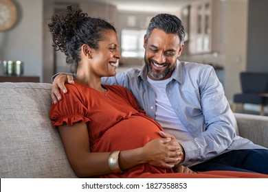 Mid adult couple expecting a baby while husband caresses the belly of his pregnant african woman. Lovely indian man touching belly of his girlfriend and feeling baby movement.
