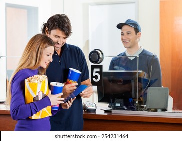 Mid Adult Couple Holding Snacks While Buying Movie Tickets At Box Office