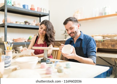 Mid adult couple smiling while doing creative painting on bowls in pottery workshop
