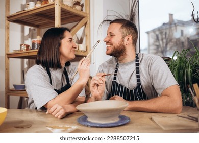 Mid adult couple smiling while doing creative painting on bowls in pottery workshop. - Powered by Shutterstock