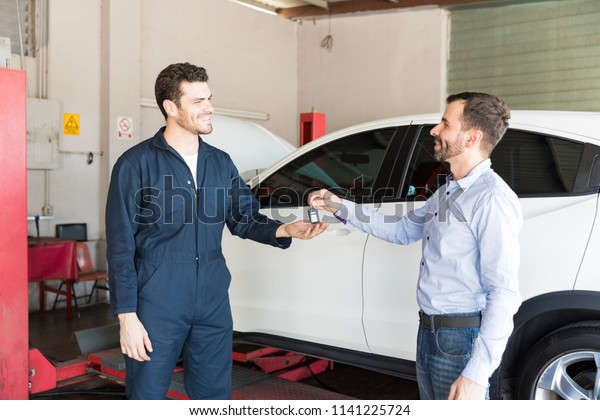 Mid adult customer handing key to male mechanic by
white car in garage