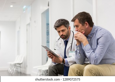 Mid Adult Doctor Explaining Serious Patient Over Digital Tablet At Hospital