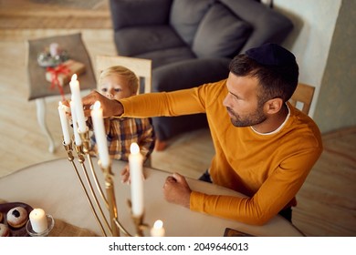 Mid Adult Father And His Small Son Lighting Candles In Menorah While Celebrating Hanukkah At Home.