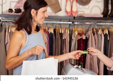 Mid adult female customer with shopping bags receiving credit card from saleswoman in boutique