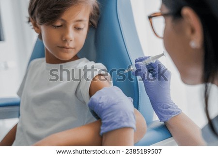 Mid adult female doctor ready to make injection to teenage boy visitor in hospital. Immunization, taking remedy drugs medicines. Vaccination against coronavirus, measles, hepatitis.
