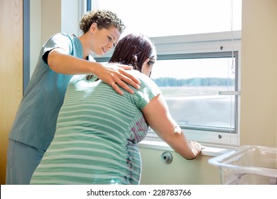 Mid adult female nurse comforting tensed pregnant woman leaning on window sill in hospital room - Powered by Shutterstock