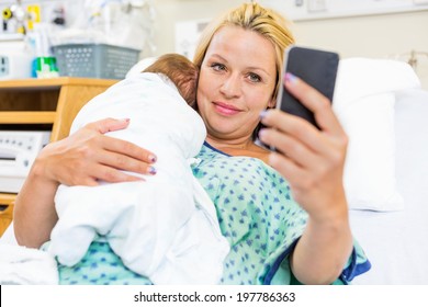 Mid Adult Female Patient Taking Self Portrait With Newborn Babygirl Through Smart Phone In Hospital Room