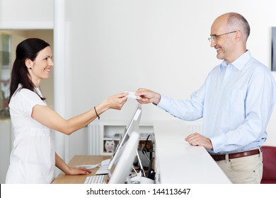 Mid adult female receptionist receiving card from patient in dentist clinic - Powered by Shutterstock