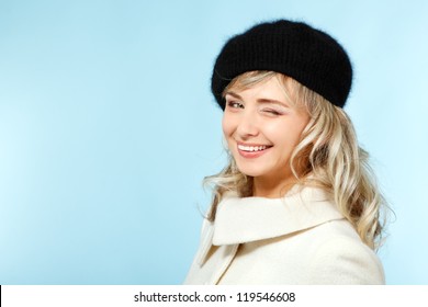 Mid Adult Happy Attractive Woman Gives A Wink, Winter Portrait Of Attractive Caucasian Middle Aged 40 Years Old Lady In Coat And Hat Over Blue