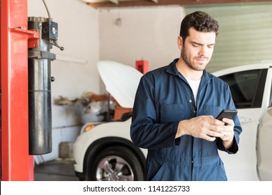 Mid adult maintenance worker using mobile phone in auto repair shop - Powered by Shutterstock