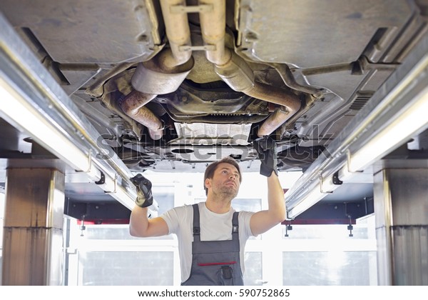 Mid\
adult male repair worker repairing car in\
workshop