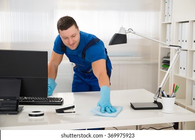 Mid Adult Male Worker Cleaning Desk With Sponge At Office