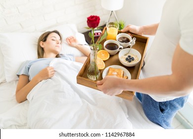 Mid Adult Man Bringing Healthy Breakfast For Sleeping Girlfriend In Bed At Home