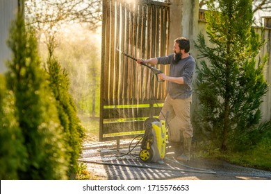 Mid Adult Man Cleaning A Wooden Gate With A Power Washer. High Water Pressure Cleaner Used To DIY Repair Garden Gate.