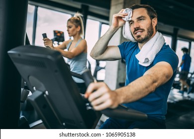 Mid Adult Man Training Hardly On Cycling Machine In Light Spacious Gym.