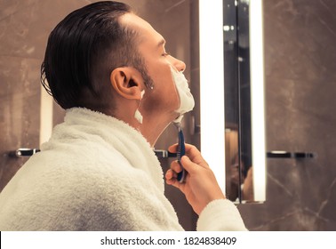 Mid adult man using razor and shaving in the bathroom.  - Powered by Shutterstock