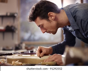 mid adult man at work as craftsman in italian workshop with guitars and musical instruments, smoothing guitar body - Powered by Shutterstock