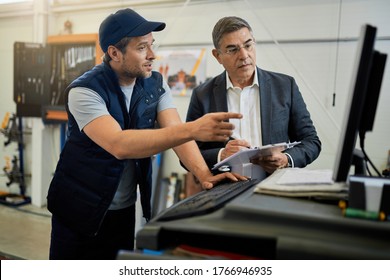 Mid adult manager and car mechanic talking while using computer in auto repair shop. 