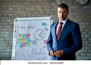 Mid adult manager holding a business presentation and looking at the camera while standing in front of whiteboard. 