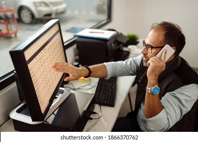 Mid adult mechanic using computer and examining data wile making a phone call in the office of auto repair shop. - Powered by Shutterstock