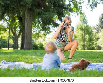Mid adult mother photographing baby boy during picnic at park
