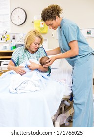 Mid adult nurse helping woman in holding newborn baby at hospital room