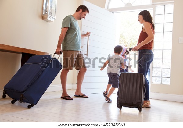 Mid adult white couple and kids\
leaving their home with luggage to go on vacation, full\
length
