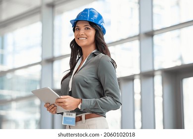Mid adult woman architect wearing hardhat at construction site while working on digital tablet. Supervisor wearing safety helmet while working in a building site. Successful and proud inspector.