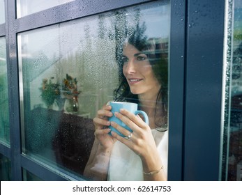 mid adult woman drinking coffee and looking out of the window on rainy day. Horizontal shape