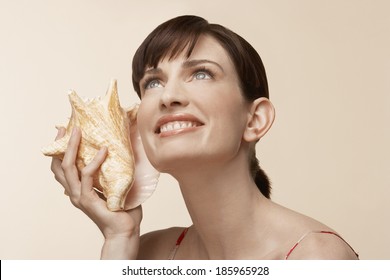 Mid Adult Woman Holding Conch Shell To Ear