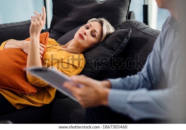 Mid adult woman lying down on\
psychiatrist\'s couch while communicating with her\
therapist.