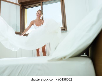 Mid Adult Woman Making Bed With White Sheet. Horizontal Shape, Low Angle View