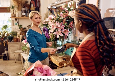 Mid adult woman paying with credit card while buying bouquet of flowers at flower shop. - Powered by Shutterstock