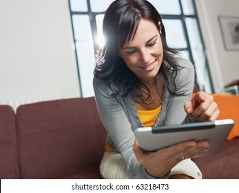 mid adult woman sitting on sofa with tablet pc. Horizontal shape, front view, copy space