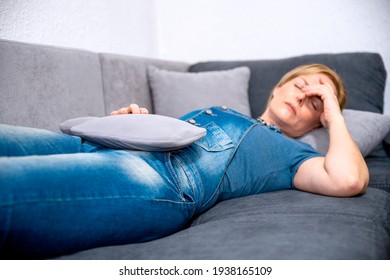 Mid Adult Woman Suffering From Stomach Cramps In Menopause Period. Woman Laying On Sofa Holding Lower Belly In Pain