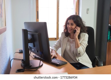Mittlere erwachsene Frau, die am Computer mit Telefon arbeitet