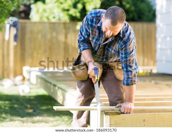 Mid adult worker sawing wood at construction site
