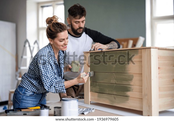 Mid adults couple painting furniture indoors\
at home, relocation and diy\
concept.
