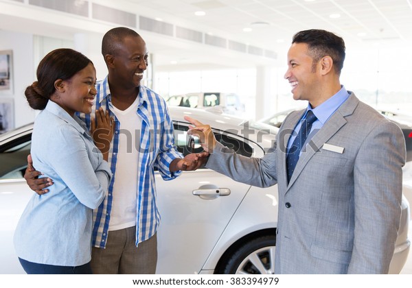 mid age car salesman handing over new car key to\
african couple in car\
showroom