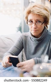 Mid Age Woman With Cell Phone Sitting At Indoor Cafe Looking In Camera