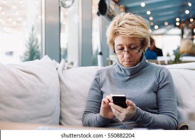 Mid Age Woman With Mobile Phone Sitting At Indoor Cafe Looking For Screen