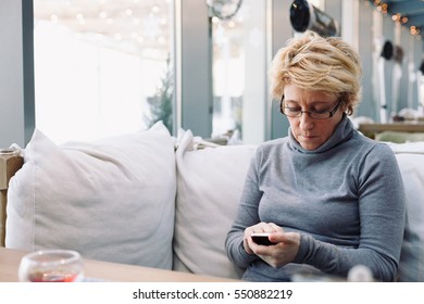 Mid Age Woman With Mobile Phone Sitting At Indoor Cafe Looking For Screen