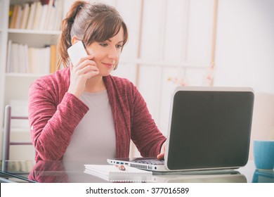 Mid Age Woman Sitting At Table With Mobile Phone And Laptop