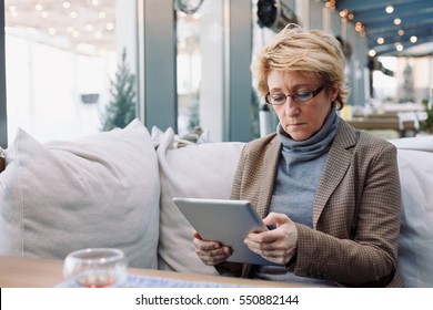 Mid Age Woman With Tablet Sitting At Indoor Cafe Looking For Screen