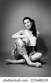 Mid Age Woman In Torn Jeans Sits On A Gray Background Monochrome