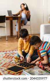 Mid Aged African American Woman Mother Working On Laptop Computer While Her Two Kids Brothers Playing At Home