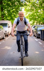 Mid aged man using a bicycle on the street. Commuter man going to work and wearing casual clothes. Full length. 